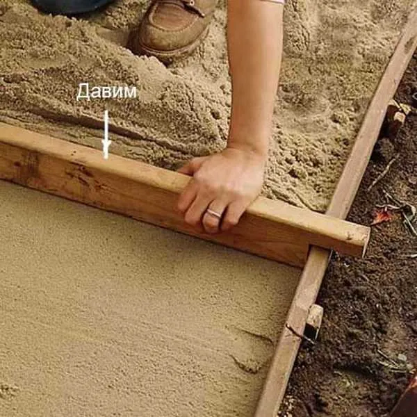 Один из способов выровнять песок под дорожку. Но необходимо вкопать предварительно доски и выставить их по уровню. Потом делают такую заготовку и песок выравнивают, протягивая ее по направляющим